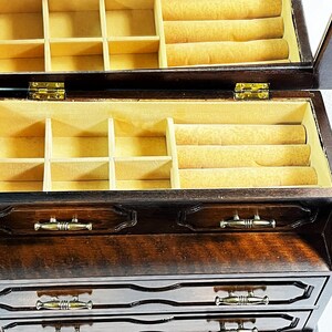 May include: A dark wood jewelry box with a hinged lid and a mirror inside. The box has four drawers and a top compartment with multiple compartments and a ring roll.
