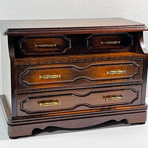 May include: A dark wood jewelry box with three drawers and brass handles. The box has a decorative carved design on the front.