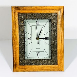 May include: A wooden framed clock with a white face and black hands. The clock face has Roman numerals and the words "QUARTZ" and "VI" on it. The frame has a decorative, ornate design.