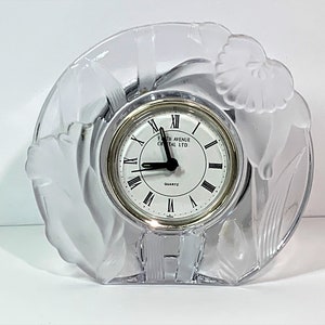 Puede incluir: Un reloj de cristal transparente con un diseño floral. La esfera del reloj es blanca con números romanos negros y las palabras "Fifth Avenue Crystal Ltd." y "Quartz".