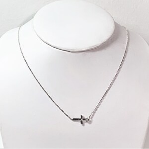 Op de afbeelding: Een zilveren ketting met een klein zilveren kruisje als hanger.