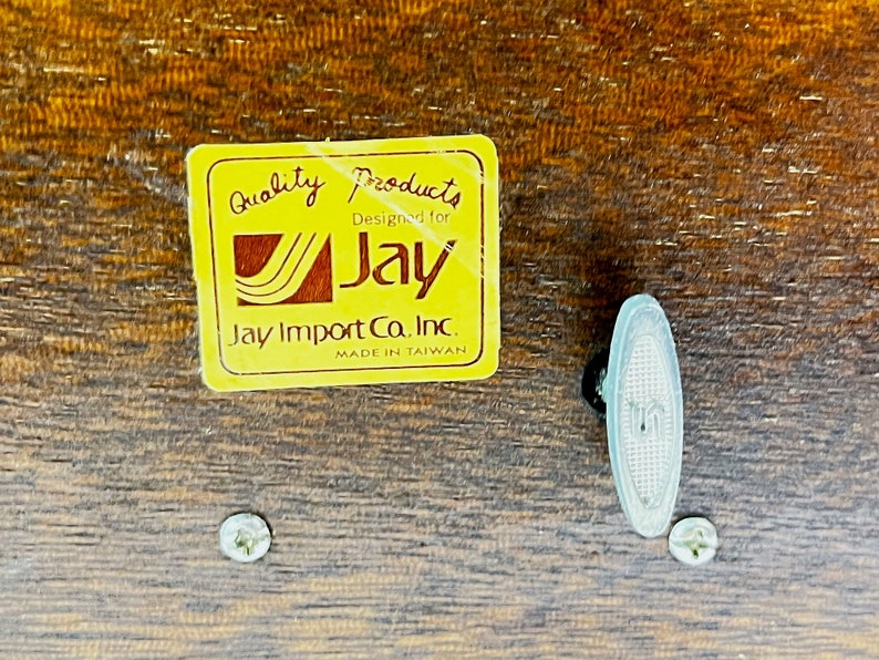 May include: A yellow label with the text "Quality Products Designed for Jay Jay Import Co. Inc. Made in Taiwan" on a wooden surface. The label has a stylized Jay logo with a wavy line design.
