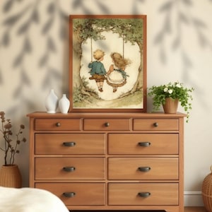May include: A framed print depicts a boy and girl on a swing under a tree. The artwork features soft colors and a vintage style. The frame is a warm brown, and the print is displayed on a wooden dresser with dark hardware. Decorative vases and a potted plant are also on the dresser.