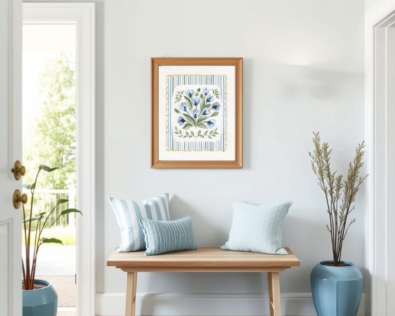 Puede incluir: Una impresi&oacute;n floral enmarcada con flores azules y verdes cuelga sobre un banco de madera con tres cojines. Los cojines son de rayas azules y blancas. Una planta alta en una maceta azul se encuentra a la derecha del banco. La habitaci&oacute;n tiene una pared azul claro y una puerta blanca.