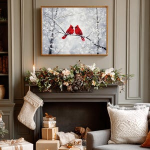 May include: A framed painting depicts two red cardinals perched on a snow-covered branch. The artwork hangs above a fireplace decorated with a garland of flowers and greenery. A Christmas stocking hangs from the mantel.