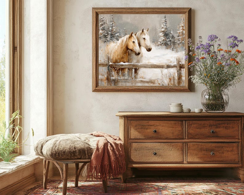 May include: A framed artwork depicts two horses in a snowy landscape, with a wooden fence and evergreen trees. The artwork hangs above a wooden dresser with four drawers. A bench with a patterned cushion and a terracotta throw blanket sits in front of the dresser.