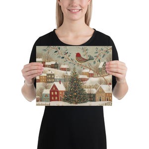 May include: A rectangular print featuring a winter village scene with snow-covered houses, a central decorated Christmas tree, and a red bird perched on a branch above. The illustration uses a muted colour palette of soft blues, reds, and browns.