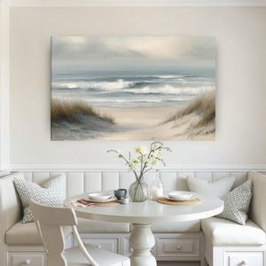 May include: A coastal landscape painting depicts a serene beach scene. The artwork features a sandy shore, rolling waves, and a cloudy sky. The painting is displayed above a white round table with a built-in bench seating area.