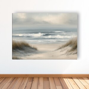 May include: A canvas print of a coastal scene. The artwork depicts a sandy path leading to the ocean, with waves crashing under a cloudy sky. Tall, dry grasses frame the path. The color palette is muted, with shades of blue, beige, and gray.