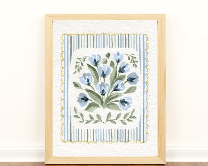 Puede incluir: Una pintura de acuarela enmarcada con un ramo de flores azules con hojas verdes. La obra de arte est&aacute; sobre un fondo de rayas verticales azules y blancas, enmarcada por un borde dorado festoneado. El marco es de madera clara.