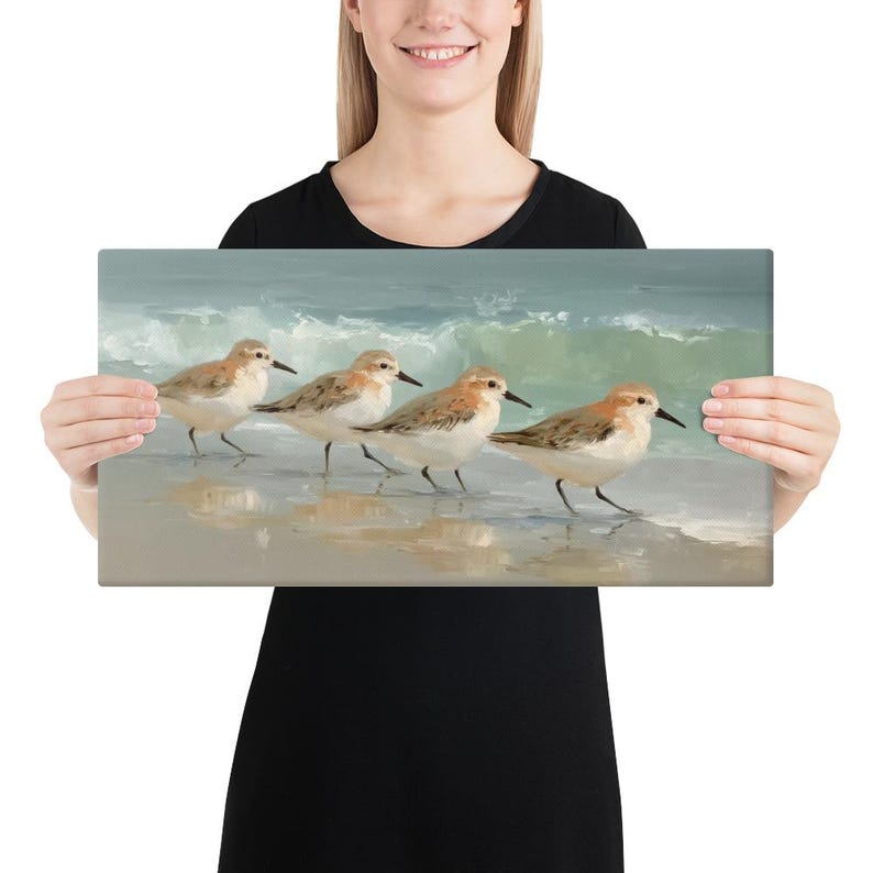 May include: A canvas print featuring four small shorebirds walking along a sandy beach with gentle waves in the background. The birds have brown and white feathers and black beaks. The artwork has a soft, muted color palette.