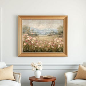 May include: A framed landscape painting with a gold-colored ornate frame. The artwork depicts a field of pink and white flowers with a soft, blurred background. Text is visible in the upper portion of the painting. The painting is displayed on a white wall.