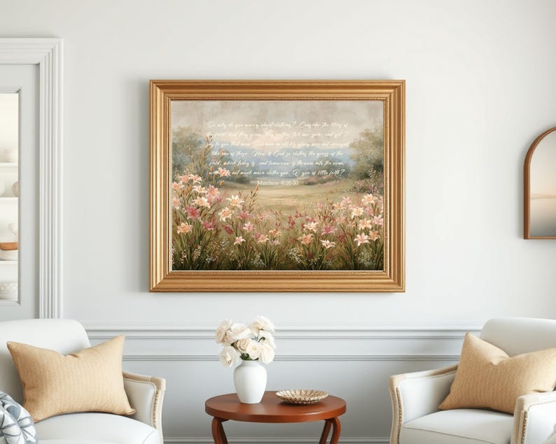 May include: A framed landscape painting with a gold-colored ornate frame. The artwork depicts a field of pink and white flowers with a soft, blurred background. Text is visible in the upper portion of the painting. The painting is displayed on a white wall.