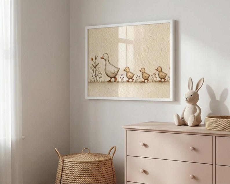 May include: A framed print featuring a mother duck and her ducklings walking in a row. The artwork is in soft, muted tones of beige, gray, and yellow. The print is displayed above a pink dresser, with a bunny figurine and a woven basket.