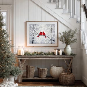 May include: A cozy interior scene featuring a framed artwork of two red cardinals perched on a snowy branch. A rustic wooden console table is adorned with candles, greenery, and woven baskets, creating a warm, inviting atmosphere. A Christmas tree is on the left.