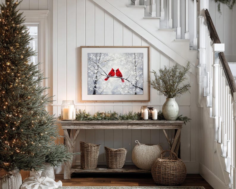 May include: A cozy interior scene featuring a framed artwork of two red cardinals perched on a snowy branch. A rustic wooden console table is adorned with candles, greenery, and woven baskets, creating a warm, inviting atmosphere. A Christmas tree is on the left.