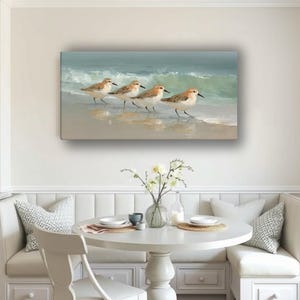 May include: A rectangular canvas print depicts four shorebirds walking along a sandy beach with gentle waves in the background. The birds have brown and white feathers, and the ocean is a mix of blue and green.