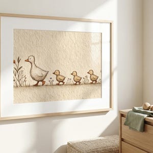 May include: A framed watercolor print of a mother duck and her three ducklings walking in a line. The artwork is in soft, muted tones of beige, brown, and white, creating a gentle, pastoral scene. The frame is a light wood.