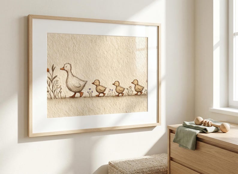 May include: A framed watercolor print of a mother duck and her three ducklings walking in a line. The artwork is in soft, muted tones of beige, brown, and white, creating a gentle, pastoral scene. The frame is a light wood.