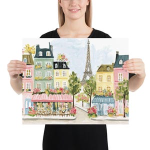 May include: A colorful print of a Parisian street scene featuring buildings in pastel colors, blooming flowers, and the Eiffel Tower in the background. The artwork depicts a cafe with a pink awning and tables.