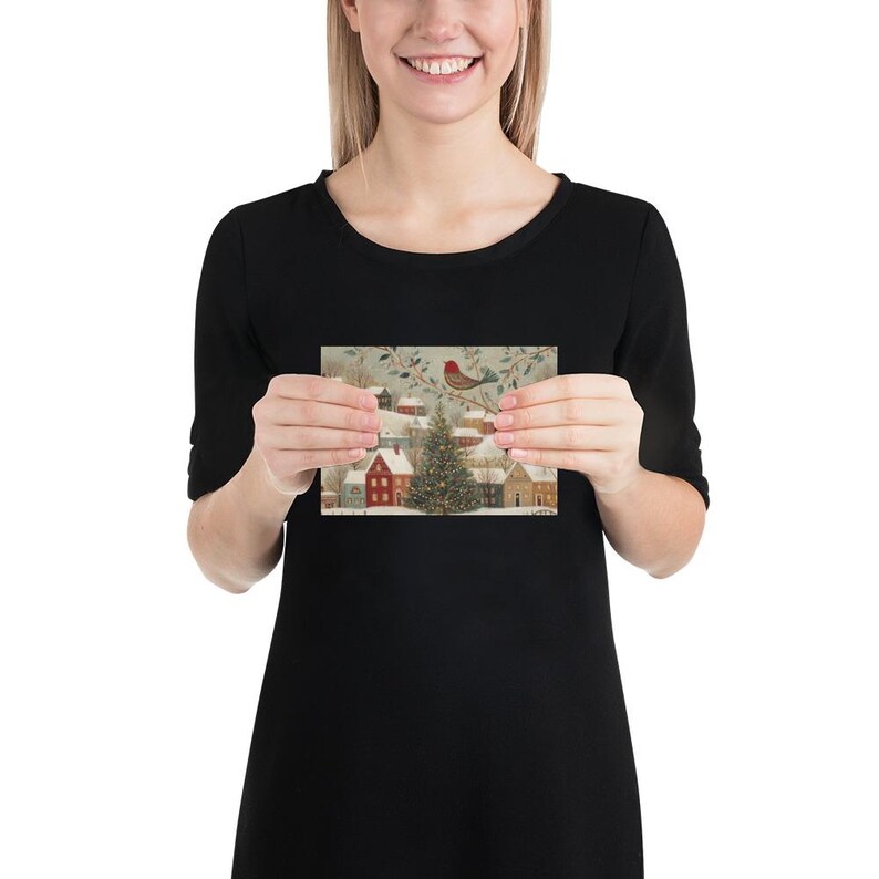 May include: A rectangular greeting card featuring a winter village scene with snow-covered houses, a central illuminated Christmas tree, and a small red bird perched on a branch above, all set against a soft, muted, and snowy landscape.