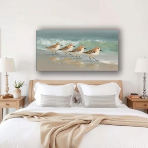 May include: A rectangular canvas print depicts four sandpipers walking along a sandy beach with gentle waves in the background. The birds have brown and white feathers, and the water is a soft blue-green.