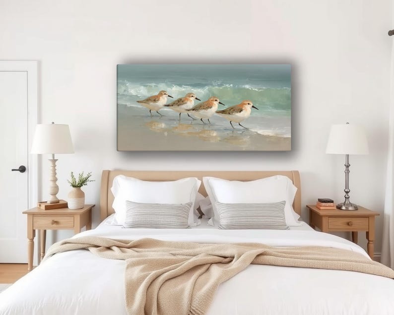 May include: A rectangular canvas print depicts four sandpipers walking along a sandy beach with gentle waves in the background. The birds have brown and white feathers, and the water is a soft blue-green.