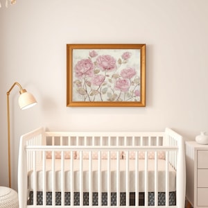 May include: A framed floral print featuring pink roses with green stems and leaves. The artwork is in a gold-colored frame and hangs above a white crib. The room also includes a white dresser, a floor lamp, and a round ottoman.