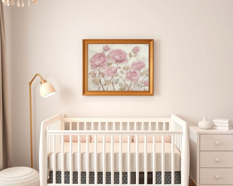May include: A framed floral print featuring pink roses with green stems and leaves. The artwork is in a gold-colored frame and hangs above a white crib. The room also includes a white dresser, a floor lamp, and a round ottoman.