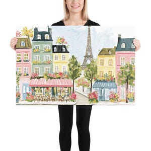 May include: A colorful painting of a Parisian street scene featuring pastel-colored buildings, cafes with pink awnings, and the Eiffel Tower in the background. The artwork depicts a charming, idyllic cityscape with trees and floral accents.