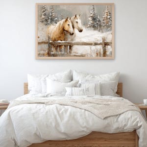 May include: A framed watercolor painting depicts two horses in a snowy landscape. One horse is light brown, the other white, standing behind a wooden fence. Snow-covered pine trees are in the background, creating a serene winter scene. The artwork is displayed above a bed.