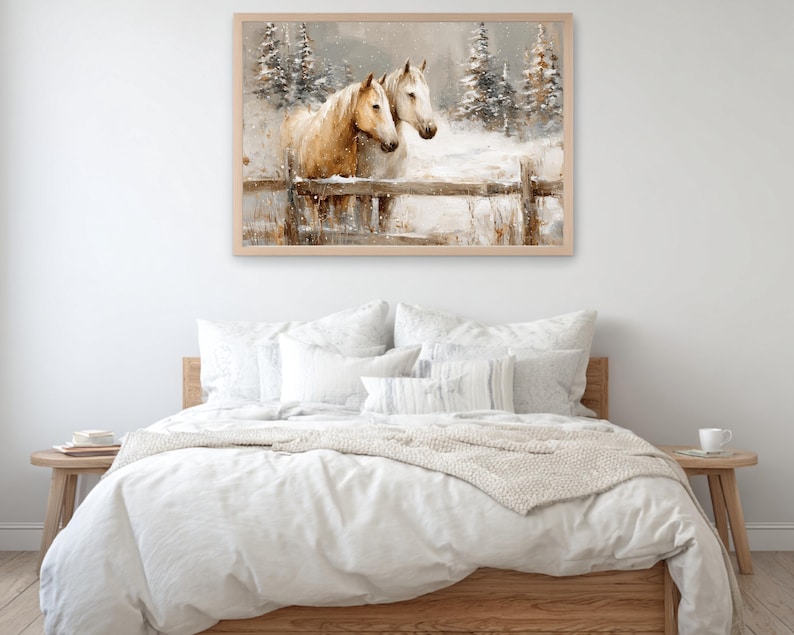 May include: A framed watercolor painting depicts two horses in a snowy landscape. One horse is light brown, the other white, standing behind a wooden fence. Snow-covered pine trees are in the background, creating a serene winter scene. The artwork is displayed above a bed.