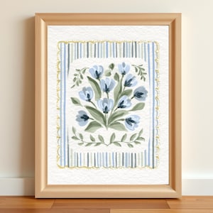 Puede incluir: Pintura en acuarela enmarcada con un ramo de flores azules con hojas verdes. El arreglo floral est&aacute; centrado dentro de un borde rectangular de rayas azules y ribete dorado. El marco es de color madera clara.