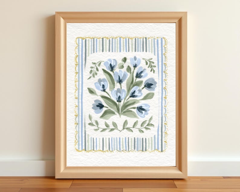 Puede incluir: Pintura en acuarela enmarcada con un ramo de flores azules con hojas verdes. El arreglo floral est&aacute; centrado dentro de un borde rectangular de rayas azules y ribete dorado. El marco es de color madera clara.