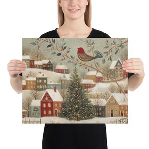 May include: A square art print featuring a winter village scene with snow-covered houses, a central decorated Christmas tree with lights, and a red bird perched on a branch in the foreground. The illustration uses a muted colour palette of red, green, and white to depict a festive holiday landscape with soft, snowy textures throughout the entire composition.