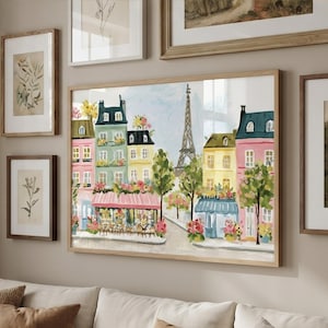 May include: A framed watercolor painting of a Parisian street scene with colorful buildings, trees, and the Eiffel Tower. The artwork is in a light wood frame and is displayed with other framed botanical prints and landscape art.