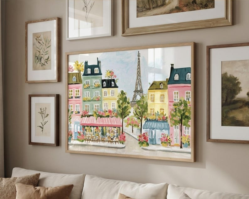May include: A framed watercolor painting of a Parisian street scene with colorful buildings, trees, and the Eiffel Tower. The artwork is in a light wood frame and is displayed with other framed botanical prints and landscape art.