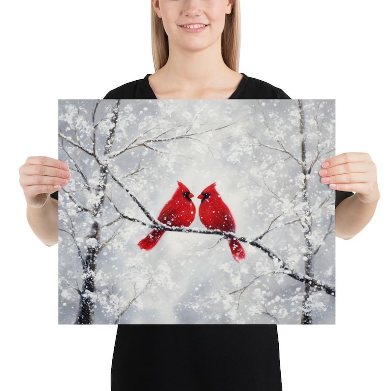 May include: A print featuring two vibrant red cardinal birds perched on a snow-covered branch. The artwork depicts a winter scene with white snow and bare tree branches against a soft, gray background. The cardinals are the focal point.