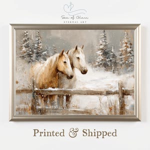 May include: A framed art print depicts two white and tan horses in a snowy landscape. The horses stand near a wooden fence, with snow-covered pine trees in the background. The artwork has a soft, painterly style.