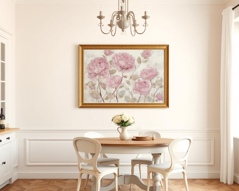 May include: A dining room scene featuring a framed floral painting with pink roses. A round wooden table is set with a vase of white flowers and tableware. White chairs surround the table, and a chandelier hangs above.