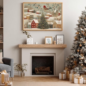 May include: A framed horizontal wall art print depicting a snowy winter village scene with colourful houses, a central decorated Christmas tree, and a red bird perched on a branch, displayed above a fireplace mantel in a living room setting.