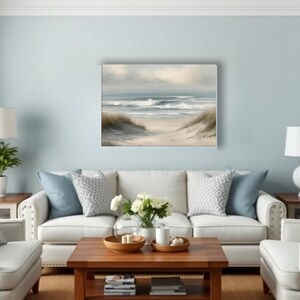 May include: A living room scene with a light blue wall, white sofa, and a wooden coffee table. A beach landscape painting hangs above the sofa. Two white lamps sit on side tables. Decorative pillows and a vase of flowers add to the decor.