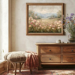 May include: A framed landscape print with a field of pink and white flowers, and text from Matthew 6:28-30. The print hangs above a wooden dresser. A bench with a patterned cushion and a terracotta throw blanket is in front of the dresser.