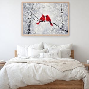 May include: A framed artwork depicts two red cardinals perched on a snow-covered branch. The painting has a winter theme with a soft, blurred background of snowy trees. The artwork is displayed above a bed with white bedding.