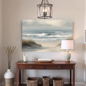 May include: A coastal-themed interior scene featuring a framed seascape painting above a dark wood console table. The painting depicts ocean waves and a sandy beach. A white lamp, decorative vase, and woven baskets complete the decor.