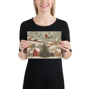 May include: A rectangular print featuring a winter village scene with snow-covered houses, a central decorated Christmas tree, and a red bird perched on a branch above. The illustration uses a muted colour palette of soft blues, reds, and browns.