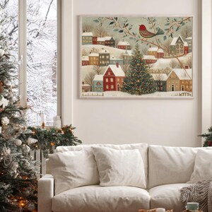 May include: A rectangular wall art print featuring a winter village scene with snow-covered houses, a central decorated Christmas tree, and a red bird perched on a branch. The illustration uses a muted colour palette of red, green, and white.