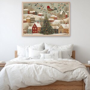 May include: A framed wall art print depicting a snowy winter village scene with colourful houses, a large decorated Christmas tree in the centre, and a red bird perched on a branch above, all rendered in a detailed, illustrative folk art style.