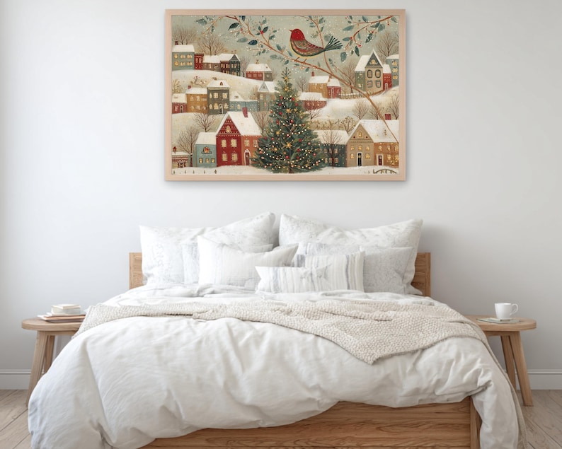 May include: A framed wall art print depicting a snowy winter village scene with colourful houses, a large decorated Christmas tree in the centre, and a red bird perched on a branch above, all rendered in a detailed, illustrative folk art style.