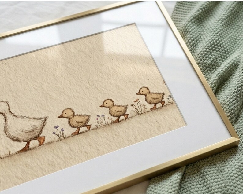 May include: A framed art print featuring a mother duck and three ducklings walking in a line. The illustration is in soft brown tones with delicate floral accents. The frame is gold-colored, and the background is a light beige.